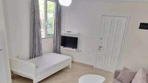 A compact living space with a sofa, a small table, a TV on a stand, and a door. - The perfect one bedroom apartment (Sarande)