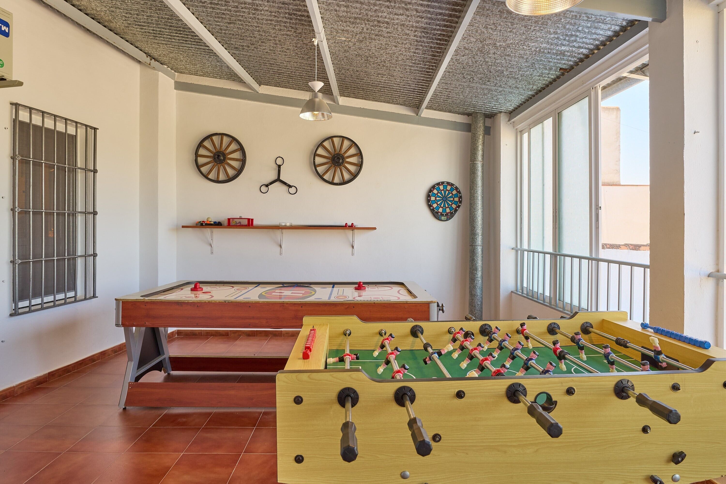 A room with a foosball table, a dartboard, and a billiards table.