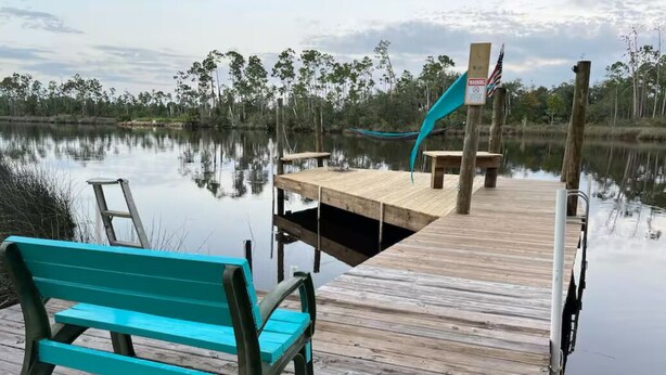 A wooden dock extending into a calm body of water, with a bench and a signpost visible. - Manatee Cove on the waterway with 5 acres. Pet Friendly. 5 minutes to the beach! (Port St. Joe)