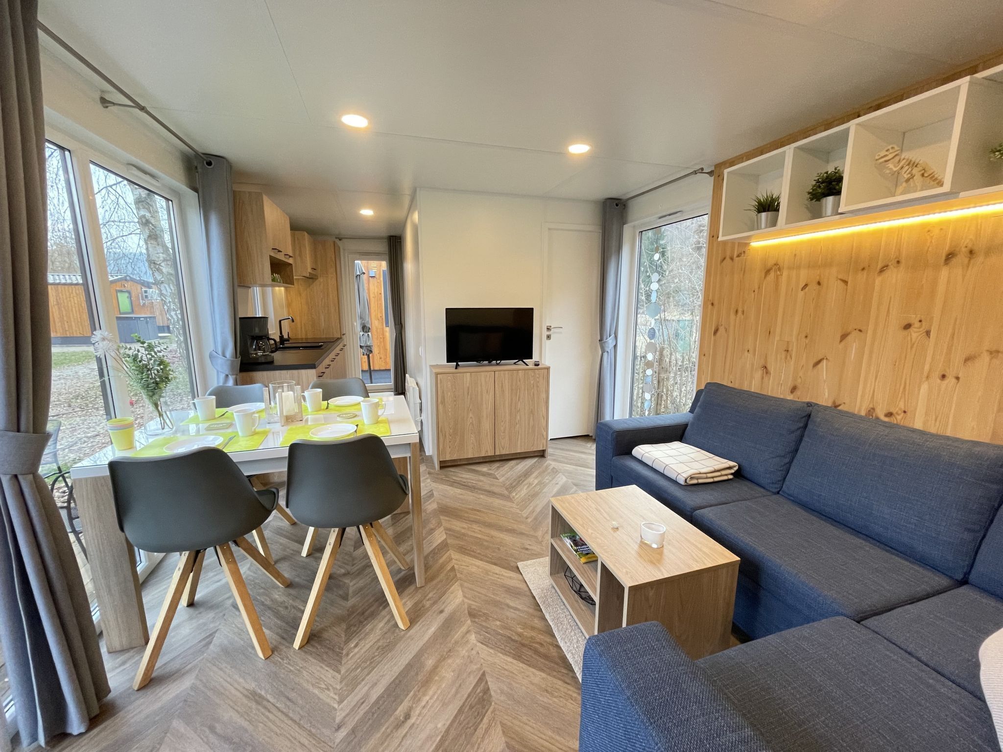 A modern living room with a sofa, a coffee table, and a dining area with chairs and a table set for two.