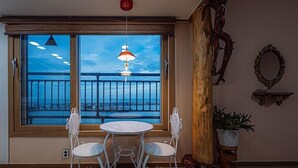 Et værelse med et stort vindue der ud til en balkon, et rundt bord med stole, en hængende pendellampe og et spejl på væggen.