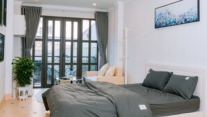 A modern bedroom with a large bed, a small table, a potted plant, and a balcony with a view.