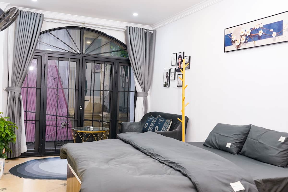 Un dormitorio moderno con una cama, una mesita y una silla. Se ve una ventana con cortinas y vistas al exterior.
