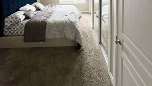 A bedroom with a sloped ceiling, a large window, a bed with a blue headboard, and a door.
