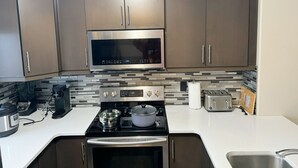 A modern kitchen with stainless steel appliances, including a microwave, stove, and oven, with a tiled backsplash and wooden cabinets.