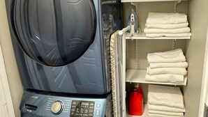 A laundry area with two stacked washing machines and a shelf with folded towels.