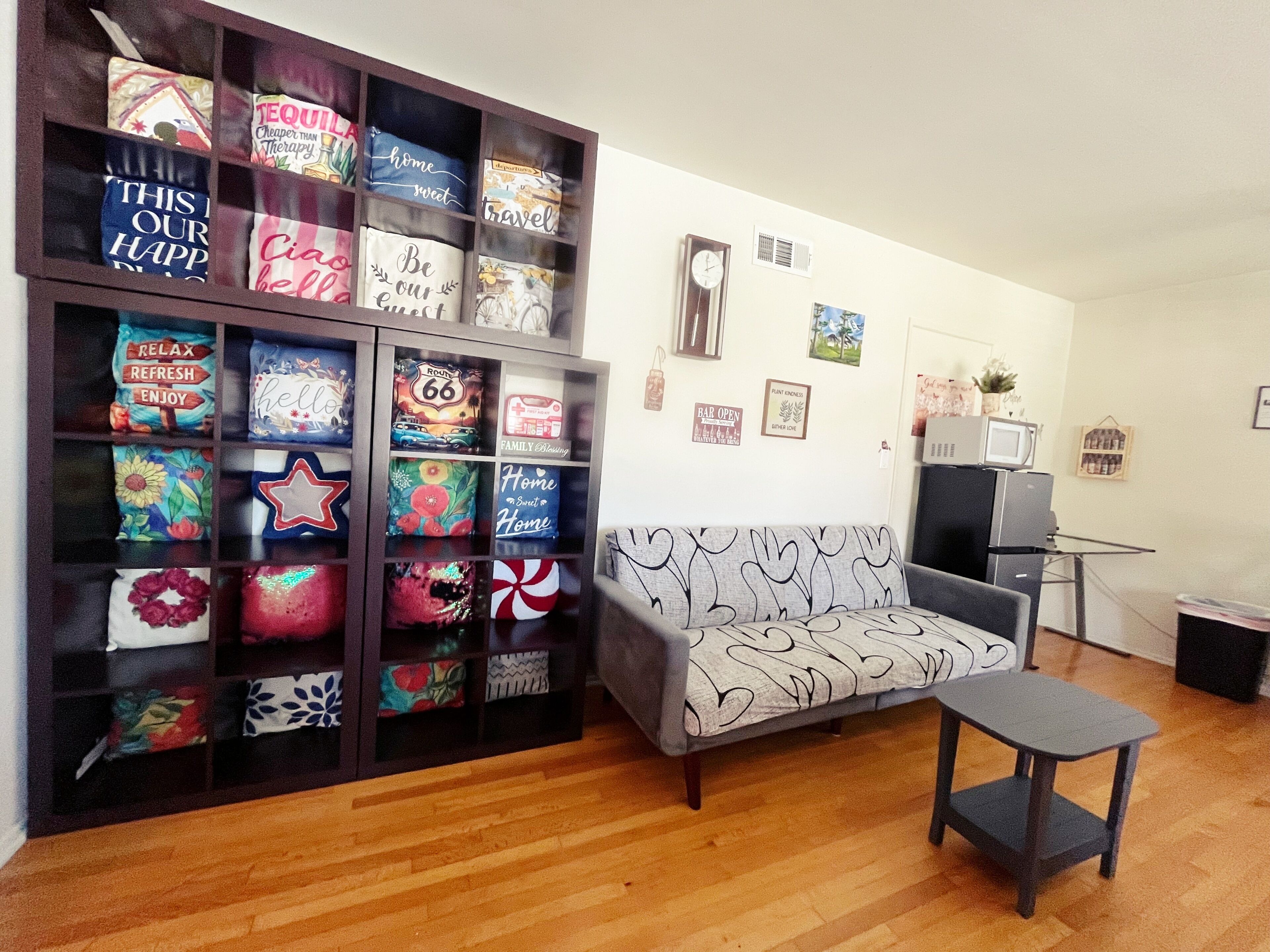 Un salon comprenant un canapé, une petite table, une bibliothèque agrémentée de coussins décoratifs et un mur orné de tableaux encadrés.
