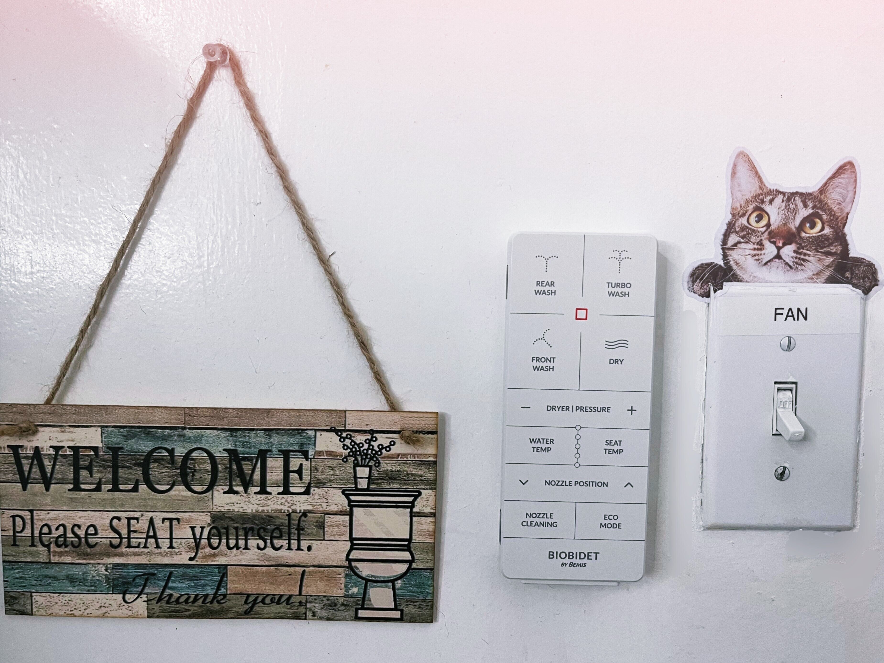 Un letrero de bienvenida con un símbolo de asiento, un panel de control con varias configuraciones y un ventilador fijado a la pared.