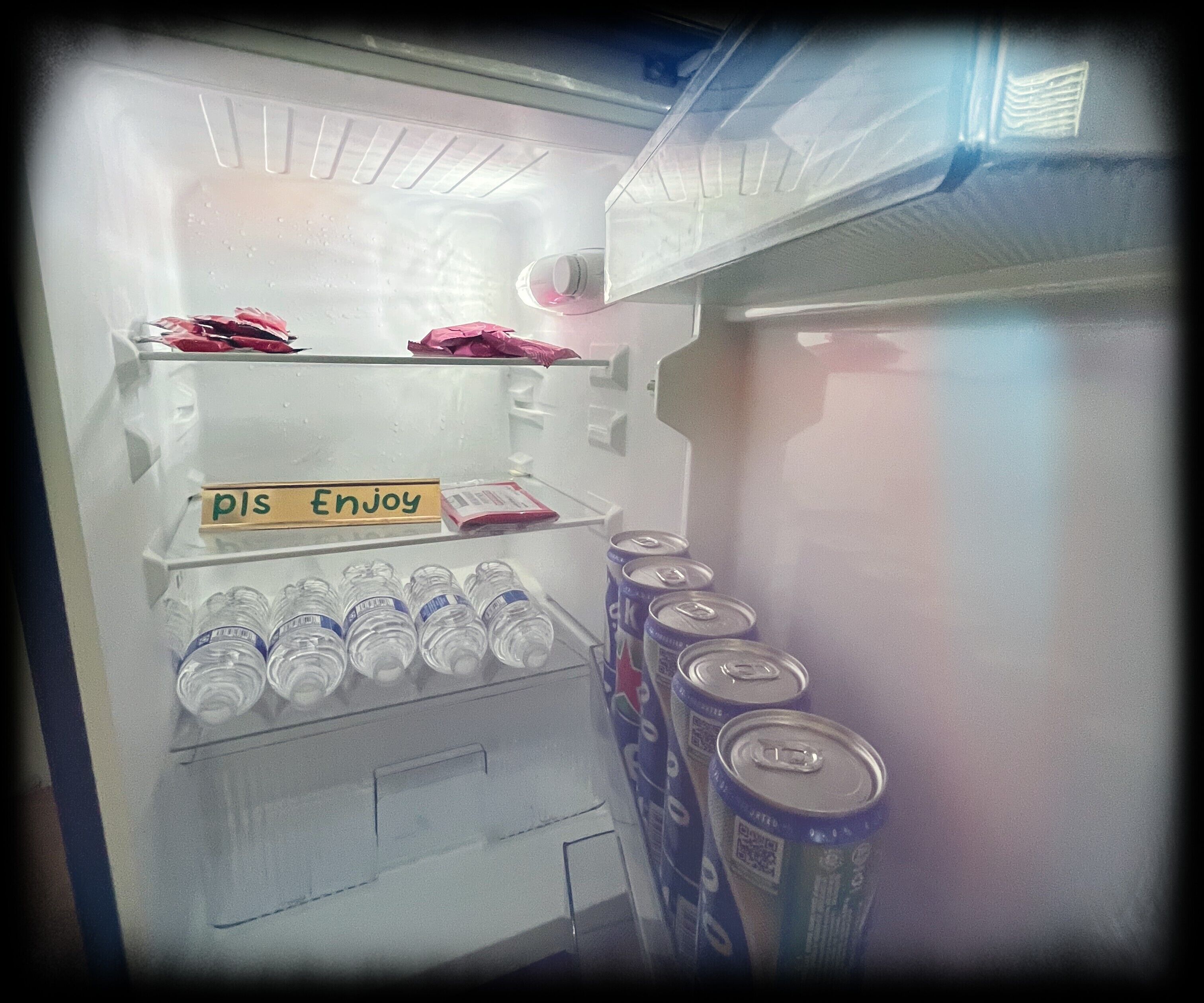 Un réfrigérateur avec une étiquette indiquant «profitez-en», des bouteilles d’eau et des canettes de soda.