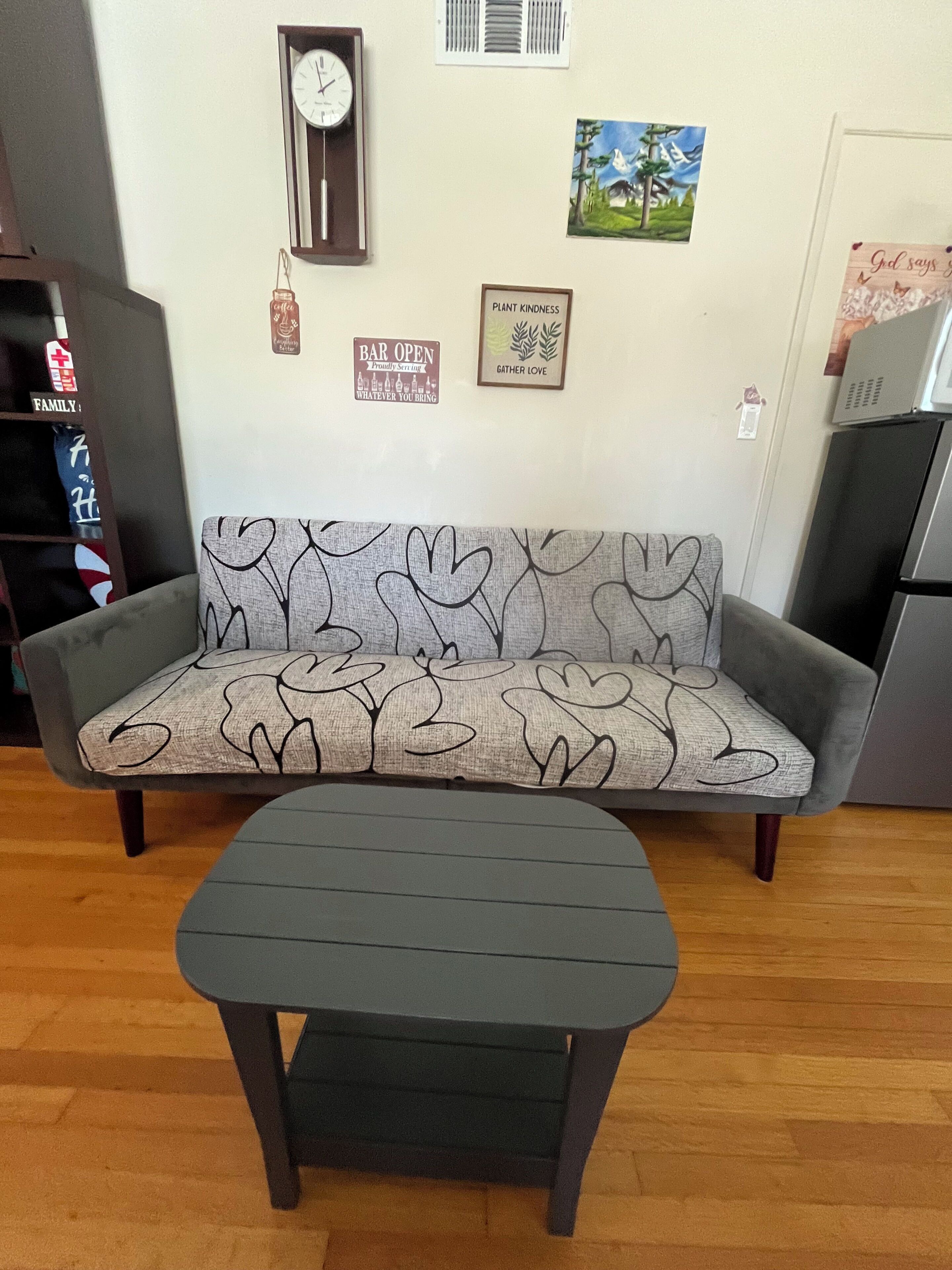 Un canapé orné d’un motif en forme de cœur, une petite table, une horloge et quelques éléments de décoration murale.