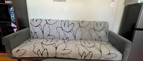Un canapé orné d’un motif en forme de cœur, une petite table, une horloge et quelques éléments de décoration murale.