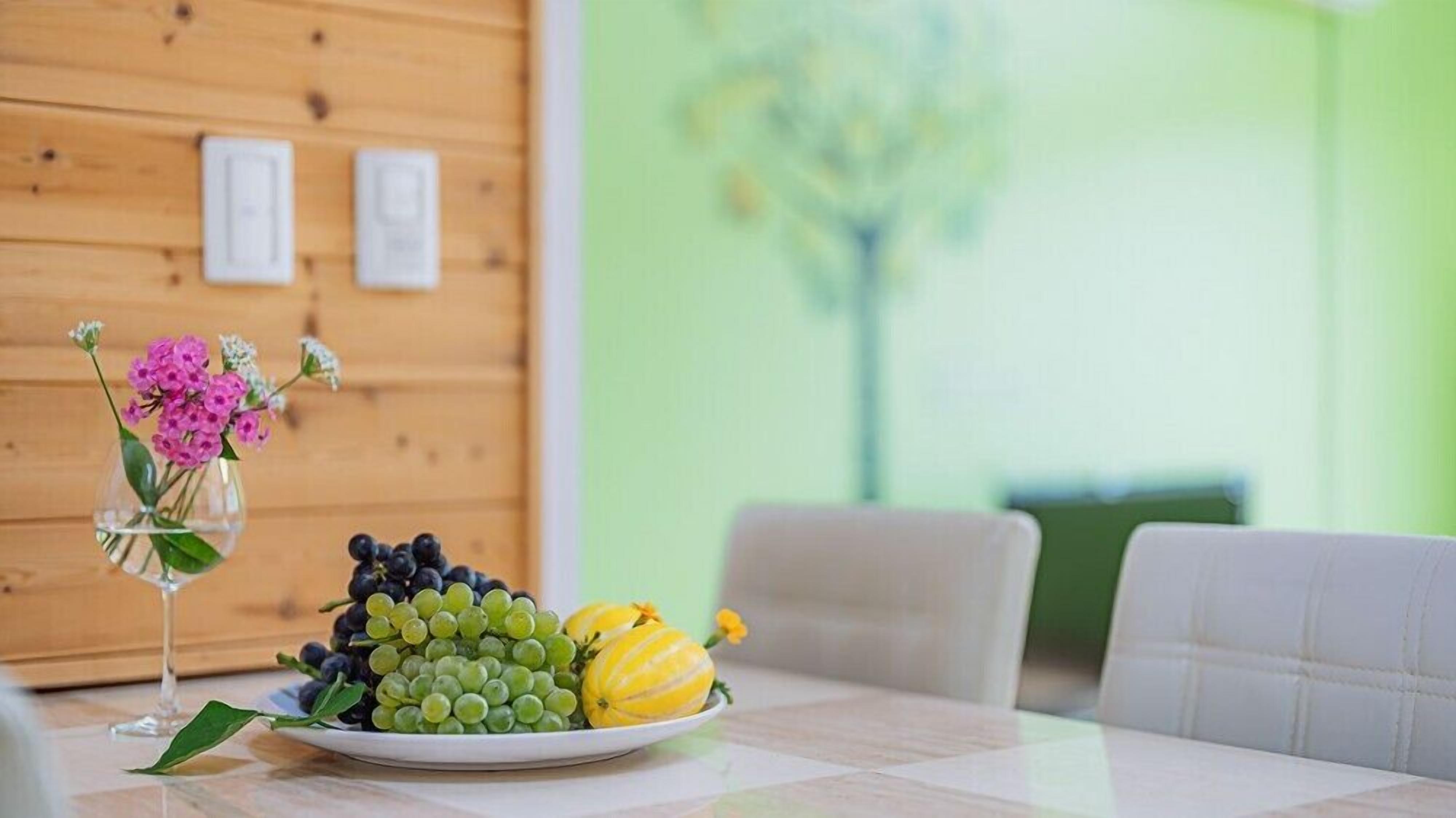Une table à manger avec une assiette de fruits et un vase de fleurs.