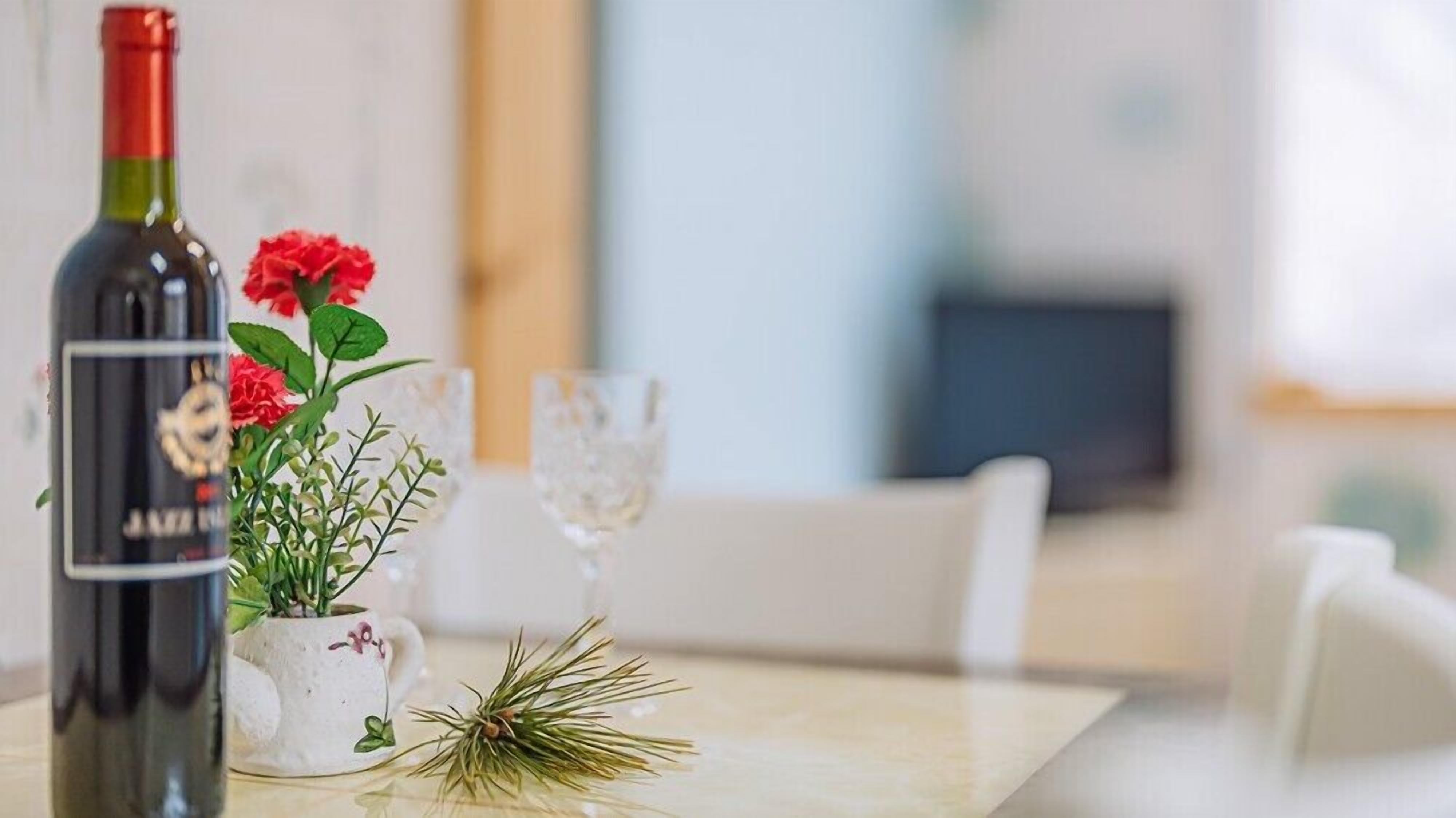 A bottle of wine, a glass, and a floral arrangement on a table.
