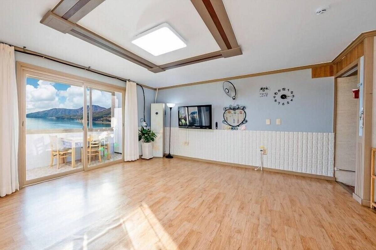 Amplia habitación con un gran ventanal corredizo que da a un balcón con vistas al mar y las montañas.