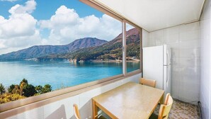 A balcony with a table and chairs, overlooking a body of water and mountains. - Haneulbada Pension (Geoje)