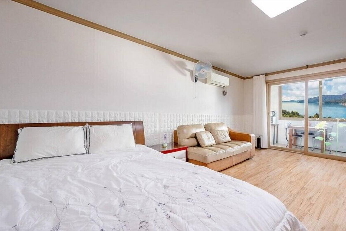 Habitación de hotel con una cama grande, un sofá, un balcón con vistas al mar y una ventana con cortinas.