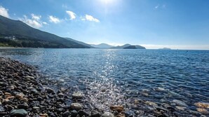 A clear lake with a rocky shoreline and mountains in the background. - Haneulbada Pension (Geoje)