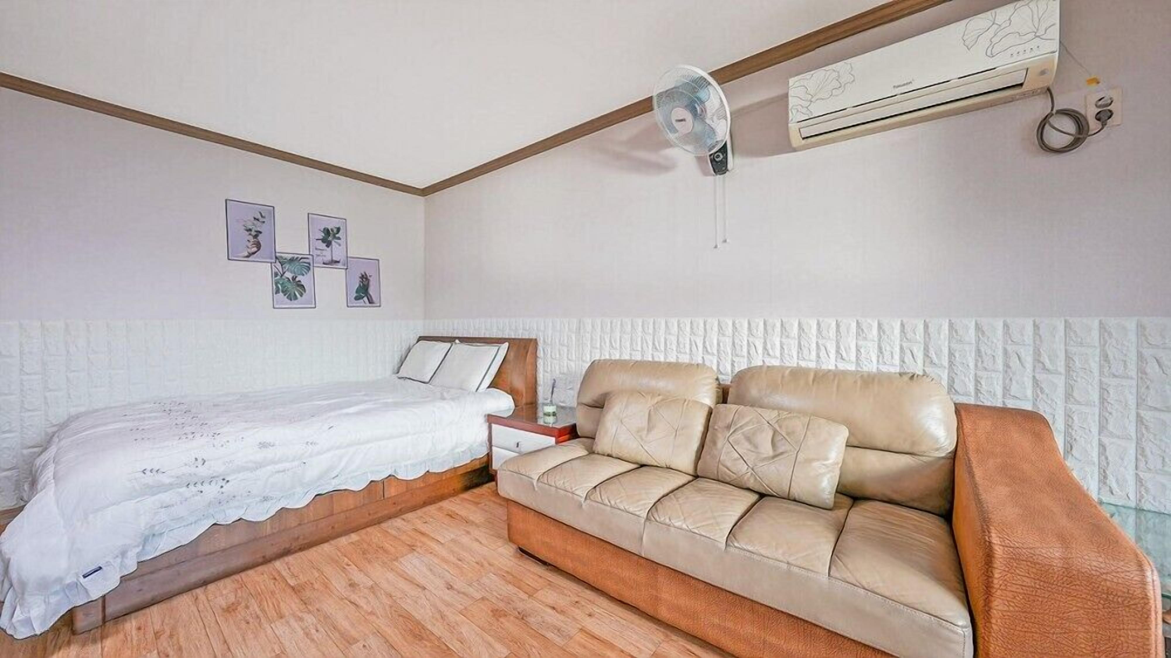 A bedroom with a bed, a sofa, a wall-mounted air conditioner, and framed pictures on the wall.