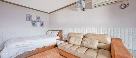 A bedroom with a bed, a sofa, a wall-mounted air conditioner, and framed pictures on the wall.