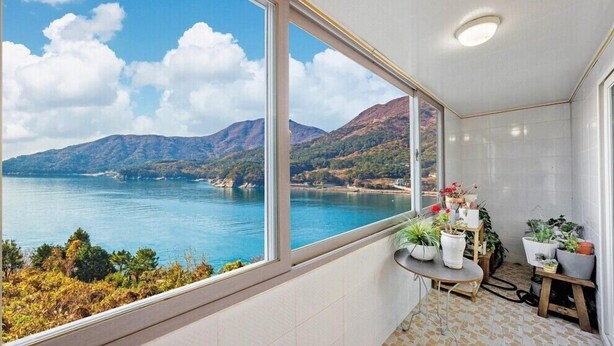 A balcony with a view of a lake and mountains, a small table with potted plants, and tiled flooring. - Haneulbada Pension (Geoje)