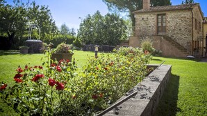 Un bâtiment en pierre avec un jardin devant, une clôture en métal et un grand arbre.