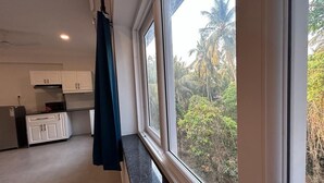 A kitchen with white cabinets, a black countertop, and a window overlooking a tropical landscape. - Serenova by Dia Hotels (Calangute)