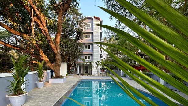 A swimming pool surrounded by potted plants and trees, with a multi-story building in the background. - Serenova by Dia Hotels (Calangute)
