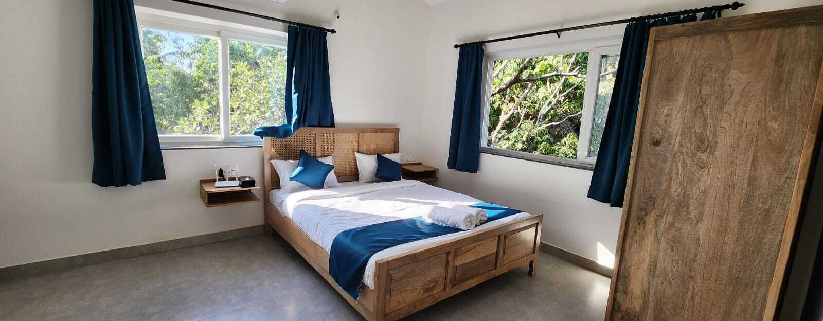 A bedroom with a wooden bed, two nightstands, a window with curtains, and a view of greenery outside.