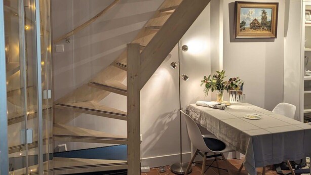 A modern interior with a wooden staircase, a dining area with a table and chairs, and a wall-mounted painting. - Het Pakhuis Haarlem - Historic House (Haarlem)