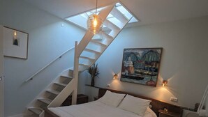 A bedroom with a skylight, a bed, a nightstand, a painting, and a staircase. - Het Pakhuis Haarlem - Historic House (Haarlem)