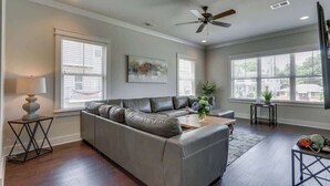 Un salon avec un canapé d’angle gris, une table basse et un ventilateur de plafond.