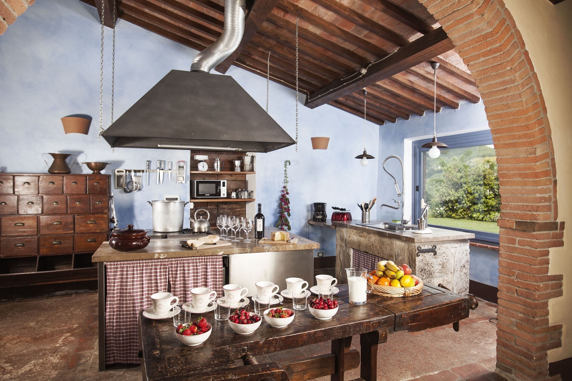 Una cucina rustica con parete in mattoni, pensili in legno e una grande isola con prodotti per la colazione.