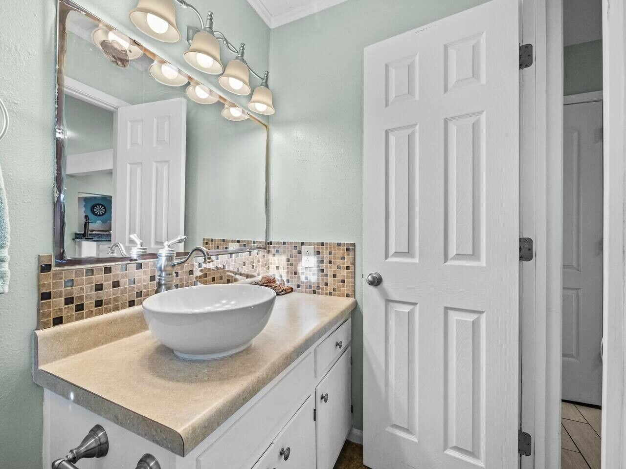 Une salle de bain avec un lavabo blanc, un miroir et une porte.