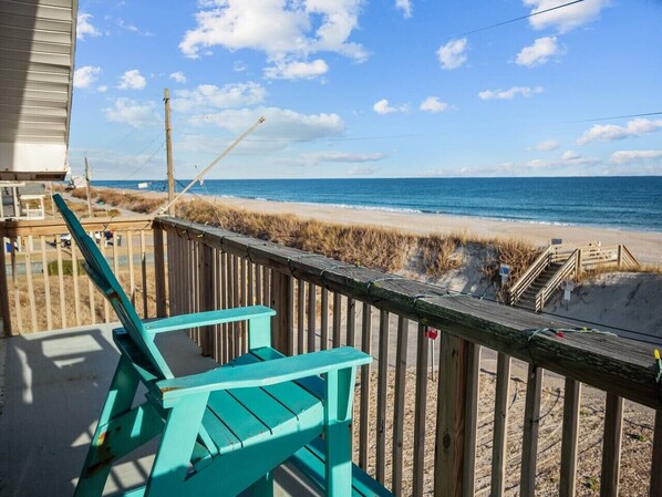 A wooden deck with turquoise chairs overlooking a beach with a wooden walkway and a stop sign.
