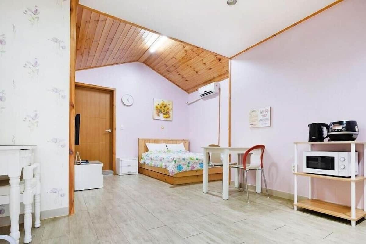 A compact room with a bed, a desk, a chair, a microwave, and a small kitchenette area.