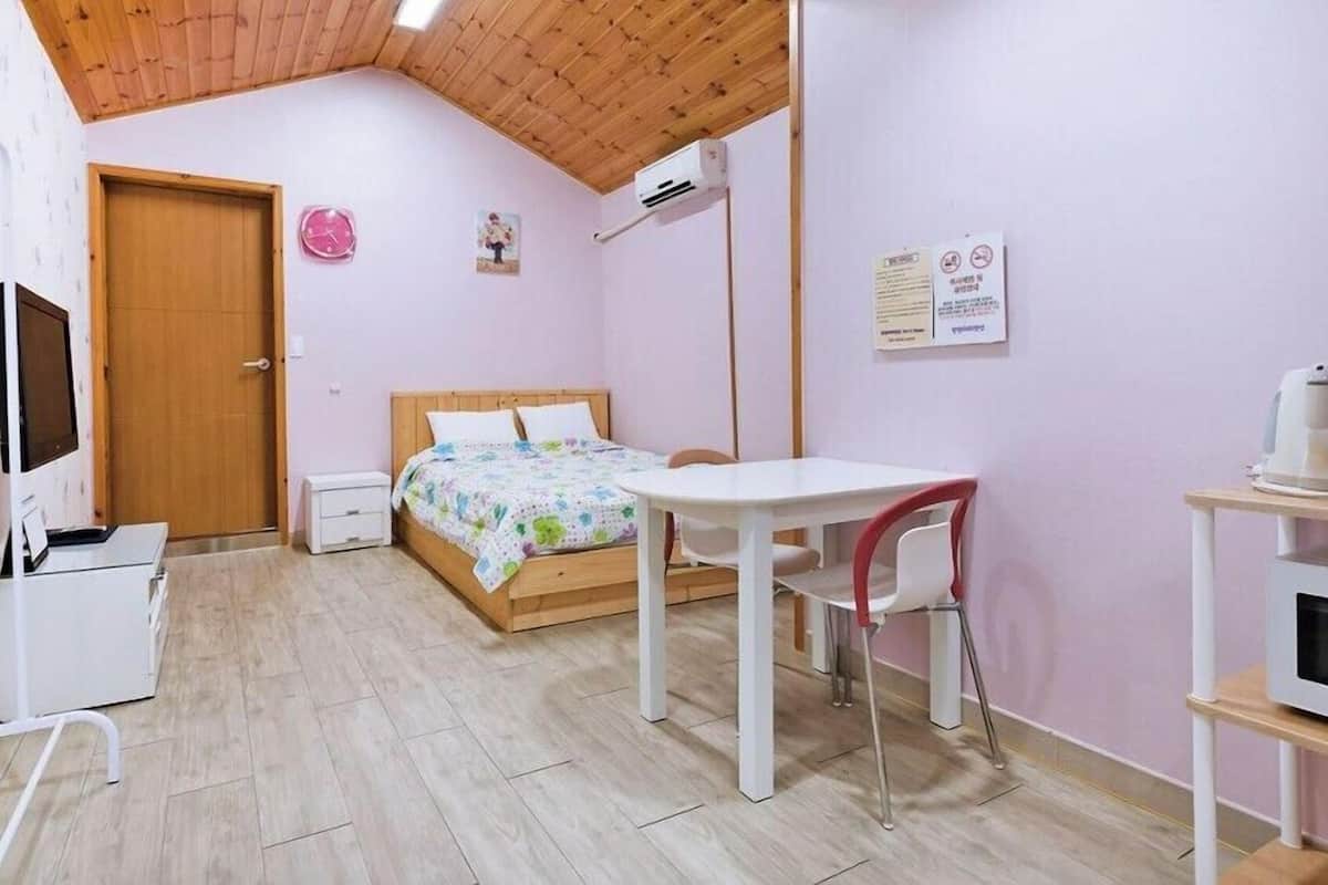 A small, cozy room with a bed, a desk, a chair, a TV, and a microwave.