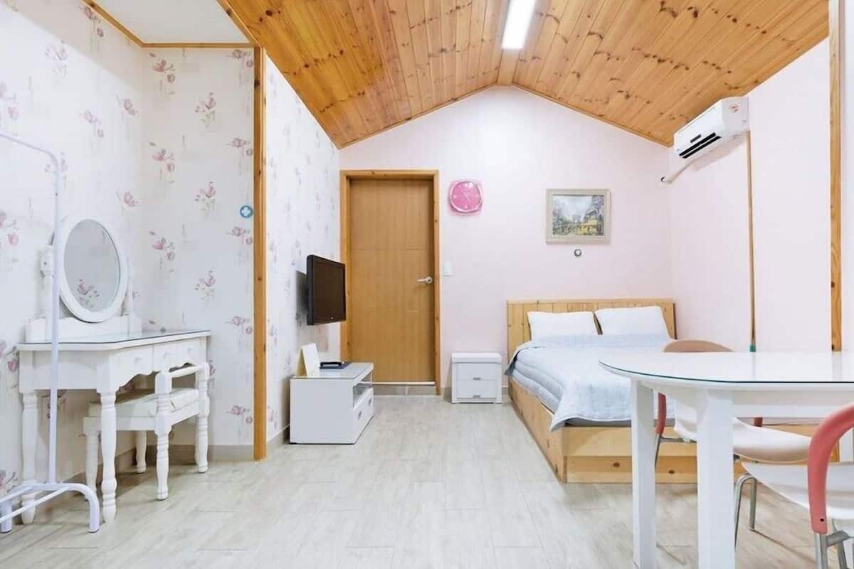 A bedroom with a wooden ceiling, a bed, a desk with a mirror, a TV, and a small table.