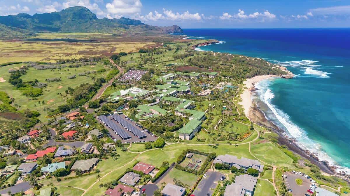 An aerial view of a coastal resort with multiple buildings, green lawns, and a beach.