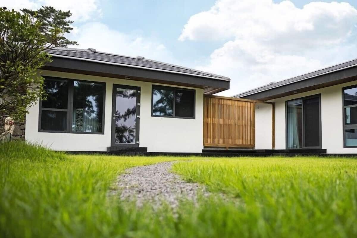 Una casa moderna a due piani con ampie finestre e una recinzione in legno al centro.