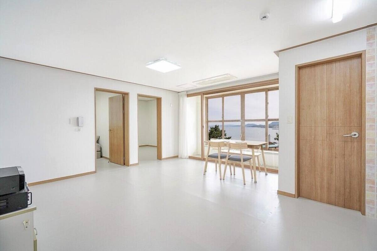 Ein geräumiger Raum mit großem Fenster, einer Holztür und einem kleinen Tisch mit Stühlen.