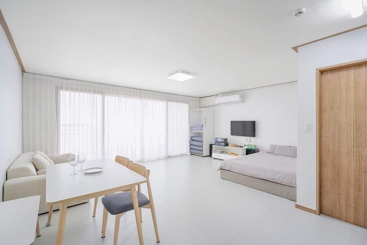Ein moderner, gut beleuchteter Raum mit Esstisch, Stühlen, einer Couch, einem Bett, einem Fernseher und einem Kleiderschrank.