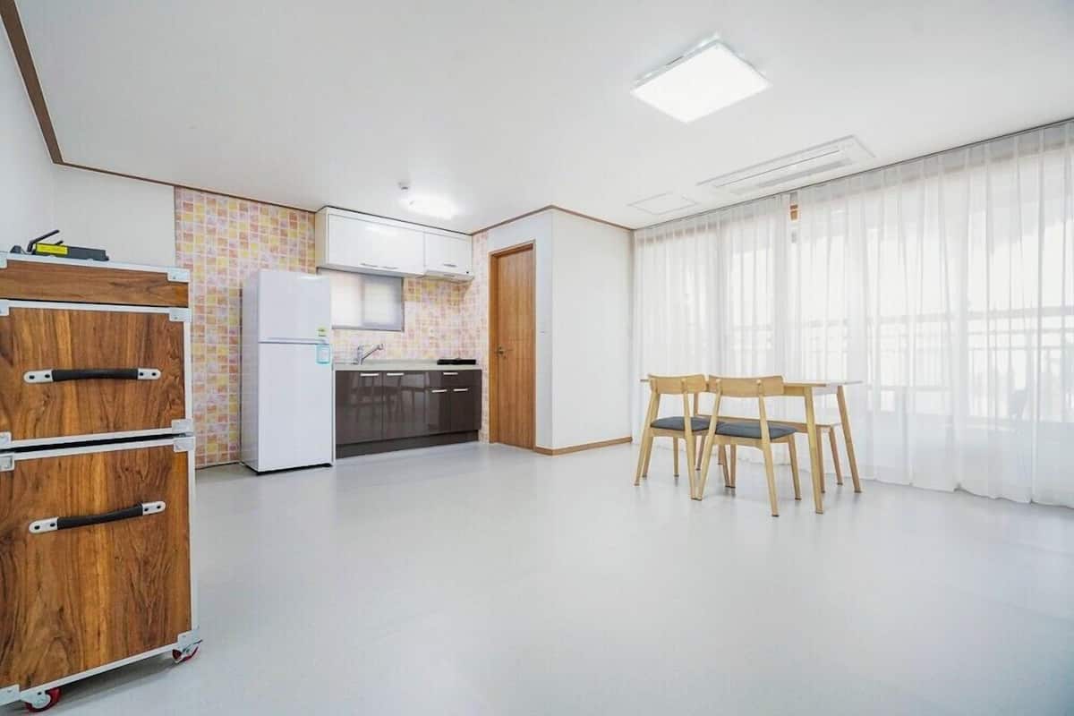 Eine moderne Küche mit weißen Schränken, einem Kühlschrank und einer gefliesten Spritzschutzwand. Ein Holzschrank mit Schubladen und ein Stuhl befinden sich im Essbereich.