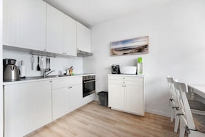 Una cocina moderna con armarios blancos, una estufa, un fregadero y una zona de comedor con mesa y sillas.