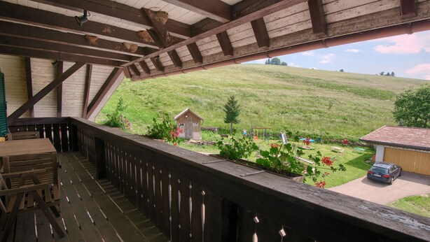 Eine Holzterrasse mit Blick auf einen grünen Hügel und ein kleines Gebäude.