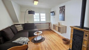 Ein Wohnzimmer mit einer Couch, einem kleinen runden Tisch, einem Kamin, einer Heizung und einem an der Wand befestigten Fernseher.