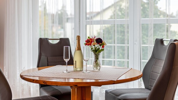 Een ronde tafel met een fles witte wijn, twee glaasjes en een bloemenvaas.