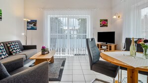 Een woonkamer met een bank, salontafel, televisie, eettafel en uitzicht door het raam.