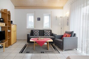 Una sala de estar con un sofá, dos sillones, una mesa de centro, un televisor y un mueble de madera.
