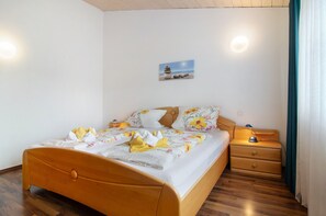Una cama bien hecha con una colcha estampada con motivos florales, una mesita de noche de madera con una lámpara y un cuadro colgado en la pared que representa una escena de playa.
