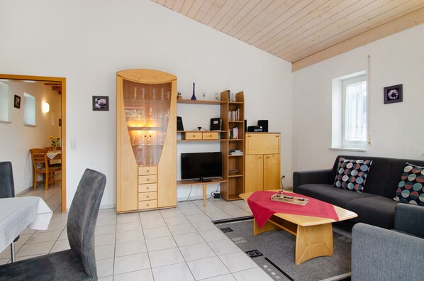 A modern living room with a sofa, a TV, a wooden cabinet, and a dining area.